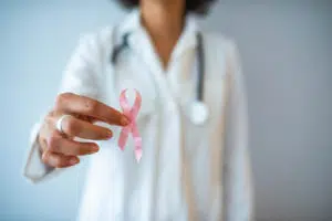 Médica segurando um laço cor de rosa como símbolo da luta contra o câncer de mama