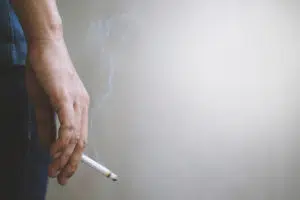 Mão de uma pessoa segurando um cigarro aceso entre os dedos