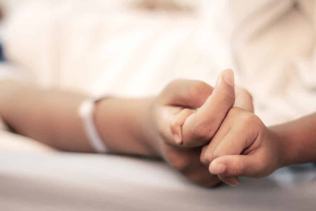 Visitante segurando a mão de paciente em hospital sob cuidados paliativos